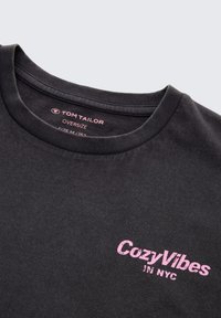 Schwarzes Oversized-T-Shirt aus weichem Stoff, mit einem pinkfarbenen Siebdruck-Logo "Cozy Vibes in NYC" auf der Vorderseite und runder Ausschnitt.