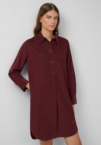 Robe chemise bordeaux à manches longues avec patte de boutonnage, col classique et fentes latérales, en tissu texturé. Design droite.