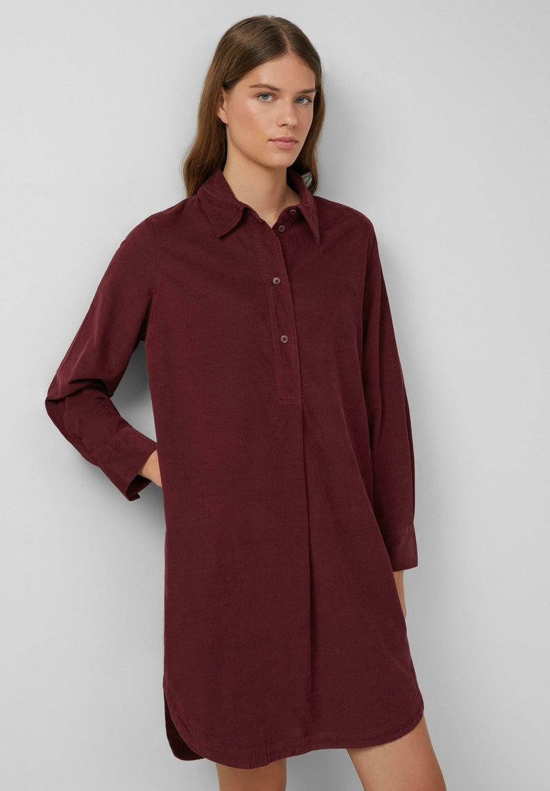 Robe chemise bordeaux à manches longues avec patte de boutonnage, col classique et fentes latérales, en tissu texturé. Design droite.