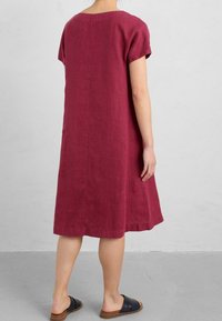 Bordeaux linneskjol med korta ärmar, avslappnad passform, knälång nederkant, synlig sömnad längs sidorna, bärs med svarta slidesandaler.