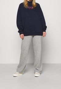 Laivastonsininen collegepaita, jossa on vaaleanpunainen "GAP"-logo, ylisuurikokoinen malli, yhdistetty vaaleanharmaihin leveälahkeisiin collegehousuihin ja kermaan sävyisiin lenkkareihin. Pehmeä kangaspinta.