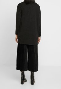 Top negro de manga larga con corte relajado, combinado con culottes negros con pliegues y botines que tienen cierres de cremallera y tacón cuadrado.