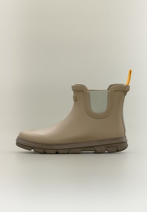 Bota de tobillo de goma beige con superficie texturizada, puntera redondeada, panel lateral elástico, lengüeta naranja y suela marrón para tracción.