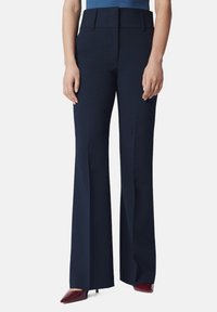 Granatowe spodnie typu wide-leg o gładkiej fakturze, wyraźnych kantach i wysokim stanem. Zestawione z szpiczastymi burgundowymi szpilkami dla kontrastu.