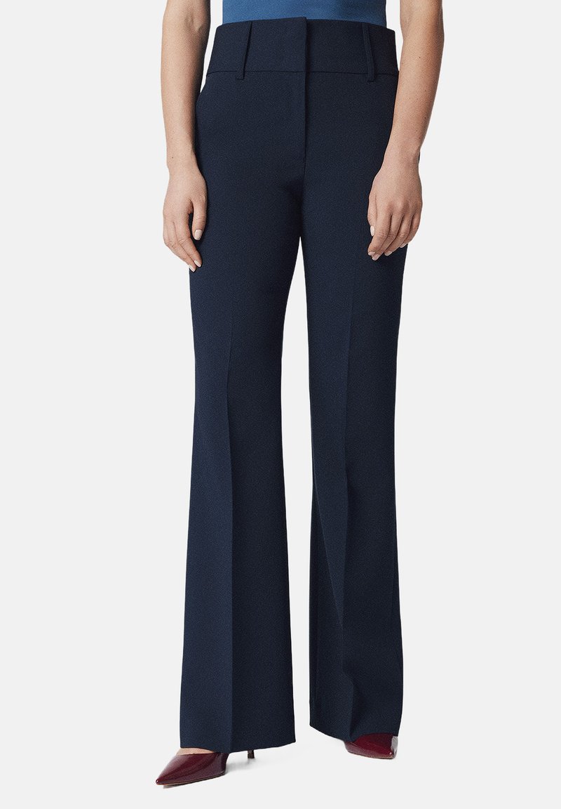 Granatowe spodnie typu wide-leg o gładkiej fakturze, wyraźnych kantach i wysokim stanem. Zestawione z szpiczastymi burgundowymi szpilkami dla kontrastu.