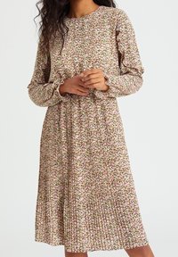 Robe à imprimé floral avec manches longues, encolure ronde, jupe plissée et tissu doux arborant des motifs roses, blancs et verts.