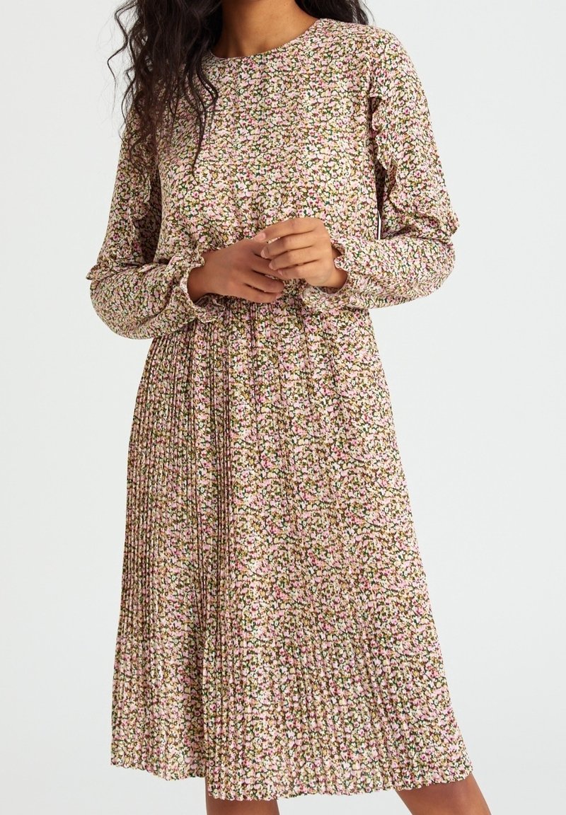 Robe à imprimé floral avec manches longues, encolure ronde, jupe plissée et tissu doux arborant des motifs roses, blancs et verts.