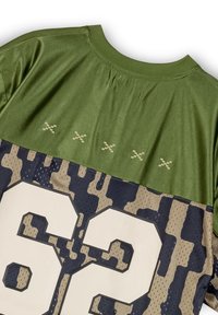 Camisa de manga corta en camuflaje verde y beige con un gran "62" blanco en la parte inferior, fabricada con un tejido texturizado y detalles de costura reforzada.