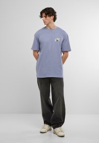 Tricou din bumbac de culoare mov deschis, cu manșete scurte, de tip crew neck și un detaliu grafic pe față. Combinat cu pantaloni largi negri și adidași.