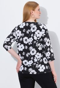 Schwarzes Oberteil mit weißem Blumenmuster, mit Dreiviertelärmeln und Rundhalsausschnitt. Weicher Stoff mit glatter Textur.