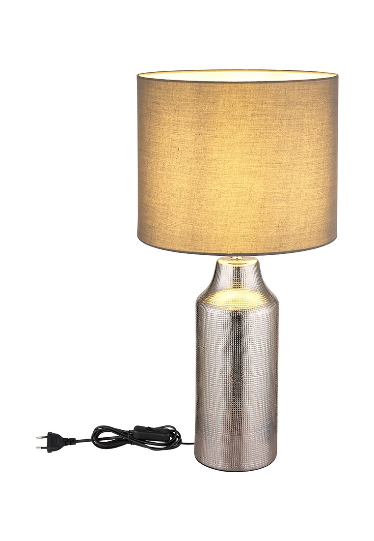 Stolní lampa s texturovanou stříbrnou základnou a béžovým textilním stínidlem. Obsahuje kulaté stínidlo, kabel a válcový tvar.