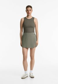 Débardeur côtelé kaki associé à une jupe drapée assortie. La tenue présente une texture lisse et un design minimaliste. Accompagnée de baskets blanches.