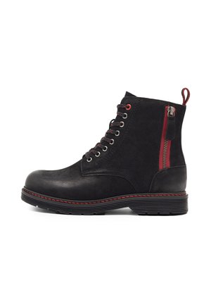Bottine noire en cuir avec des accents rouges, une fermeture éclair sur le côté, un bout arrondi et une finition texturée. Dispose d'une semelle contrastante avec des coutures.