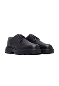 Chaussures en cuir noir avec une finition texturée, bout rond, lacets et semelle en caoutchouc épaisse avec un motif de crampons prononcé.