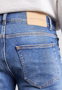 Vybledlé modré džíny z denimu s texturovan ým povrchem, na zadní straně s koženou nášivkou označenou "TIGER OF SWEDEN".