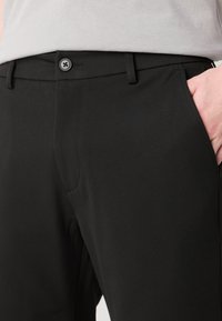 Pantalons noirs présentant une texture de tissu lisse, une coupe droite, des poches latérales et une fermeture à un bouton à la taille.