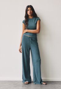 Teal ribbad stickad matchande set som består av en figurnära kortärmad topp och lösa, raka byxor med dragsko i midjan. Flip-flops fulländar looken.