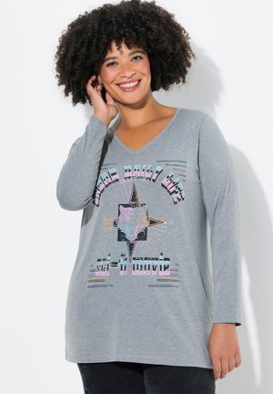Grijze langslavige T-shirt met V-hals, voorzien van kleurrijke grafische tekst en een gezichtontwerp in het midden. Lichtwijde fit.