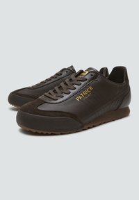 Zapatos deportivos marrones con materiales de cuero y ante, con diseño de cordones, acentos de logo dorado y suela de goma texturizada.