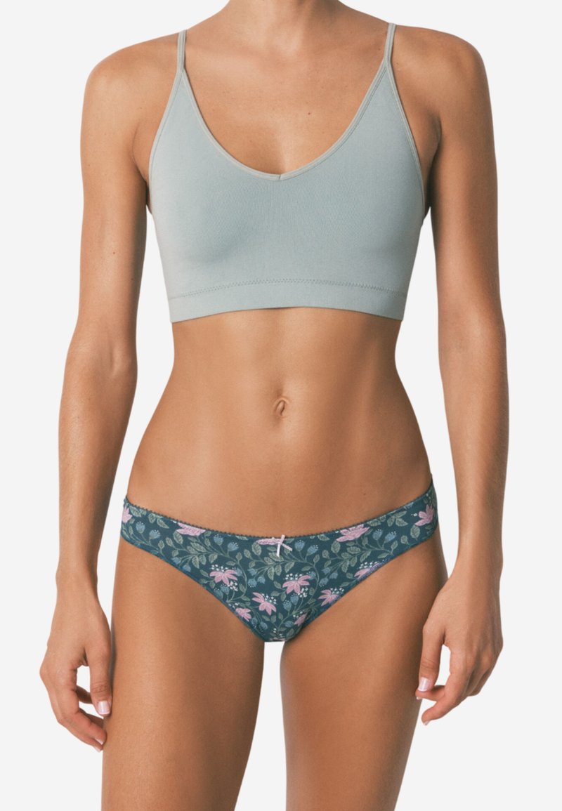 Bralette azzurro chiaro senza cuciture con scollatura a V profonda e spalline sottili, abbinato a bikini con parte inferiore floreale scura caratterizzata da motivi rosa e verdi.