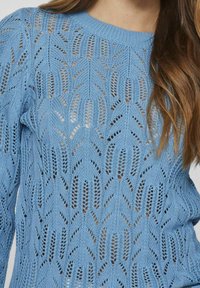Light blue knitted sweater featuring a textured, open-weave pattern with a round neckline. Long sleeves and a relaxed fit.