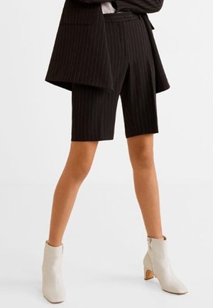 Shorts noir à rayures fines avec un design ajusté, dotés de passants de ceinture et d'une longueur jusqu'au milieu de la cuisse. Associés à des bottines crème.