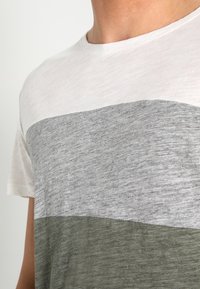 Camiseta de manga corta con tres rayas horizontales en gris claro, gris oscuro y verde oliva. Tejido suave con un cuello redondo.