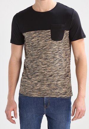 Homme portant un t-shirt à manches courtes noir et marron texturé en blocs de couleurs avec une poche poitrine noire et un jean bleu.