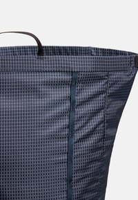 Mørkeblå stoffveske med et geometrisk diamantmønster, med en mørkeblå vertikal stripe og et svart håndtak. Teksturert overflate.