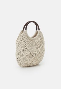 Sac à main en macramé beige avec un motif en losanges et des poignées circulaires en bois foncé sur un fond blanc.