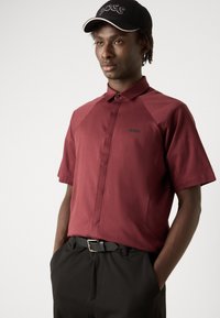 Burgundska polo majica kratkih rukava s ovratnikom na dugme i crnim "BOSS" logotipom na prsima; uparen s crnim hlačama i remenom.