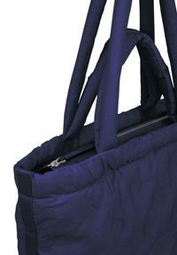 Jūras spēku krāsas kviltota soma ar divām izturīgām auduma rokturām, ar rāvējslēdzēja aizdari un teksturētu virsmu. Kompakta taisnstūrveida forma.