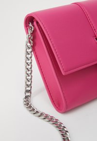 Kompakt rosa skinnveske med sølvfarget kjedeholder, med klafflås og glatt tekstur. Enkel, moderne design.