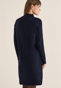Abito in maglia di colore blu navy con scollatura alta, maniche lunghe con dettagli a treccia e orli a coste. Texture morbida.