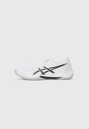Zapatilla deportiva blanca con rayas negras y suela gris, vista de lado sobre un fondo gris claro liso.