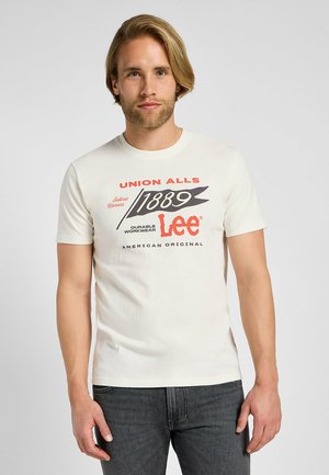 T-shirt in cotone color crema con maniche corte, caratterizzato da una stampa grafica in rosso e nero. Il testo include "UNION ALLS" e "Lee American Original."