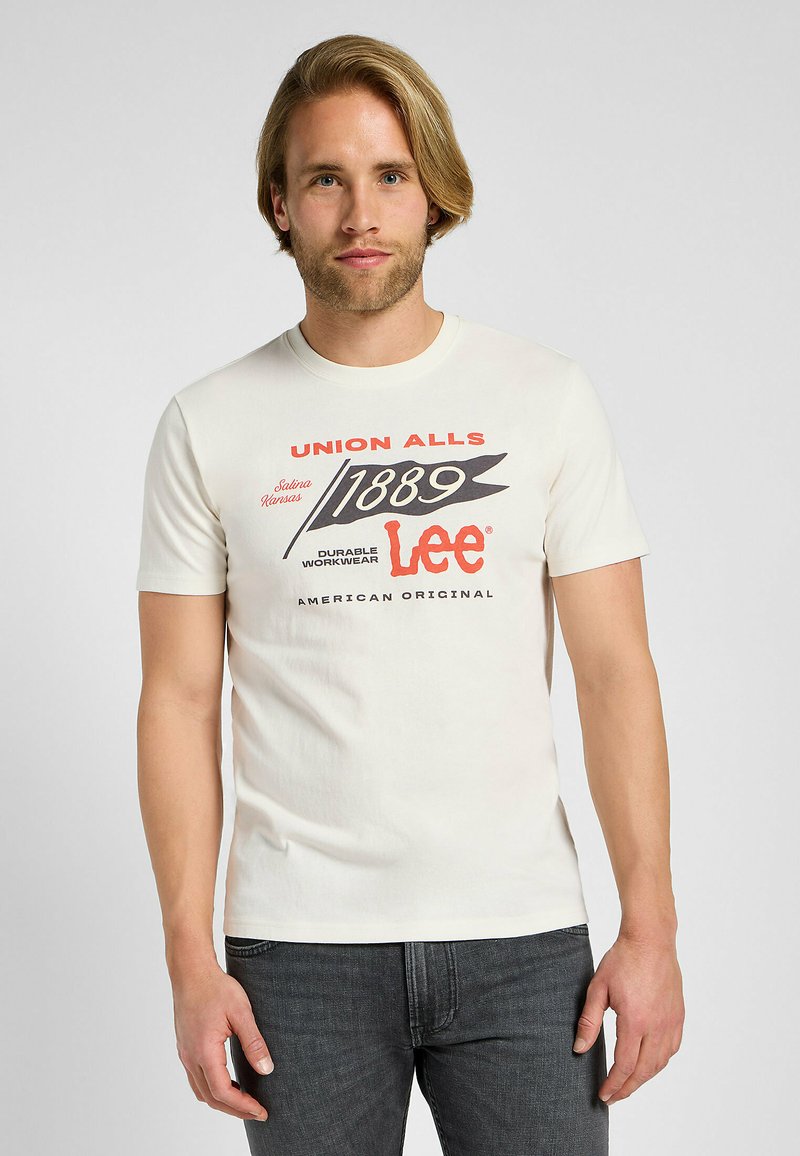 Camiseta de algodón color crema con mangas cortas, que presenta un estampado gráfico en rojo y negro. El texto incluye "UNION ALLS" y "Lee American Original."