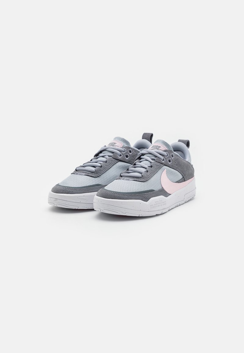 Baskets de sport grises avec tige en mesh, accents en daim et logo swoosh rose ; semelle en caoutchouc blanche et lacets plats.
