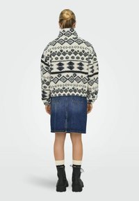 Fleece jakna s visokim ovratnikom, s geometrijskim uzorkom u crnoj i bijeloj boji, u kombinaciji je s trapero suknjom i crnim čizmama s vezicama.