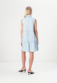 Ανοιχτό μπλε τζιν κίτρινο φόρεμα χωρίς μανίκια με μαζεμένη μέση και πολυεπίπεδη φούστα, διαθέτοντας κολάρο και χαλαρή εφαρμογή, συνδυασμένο με μαύρες σανδάλιες με τακούνι.