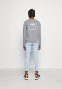 Graues Langarmshirt mit weißem Berglogo und dem Schriftzug "FUJITRAIL" auf der Rückseite, kombiniert mit hellblauen Leggings und schwarzen Sportschuhen.