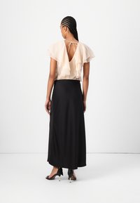 Blouse en pêche à volants avec une grande ouverture dans le dos, associée à une jupe noire longueur sol et des talons noirs avec des accents dorés.