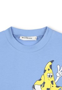 Gaiši zils kokvilnas T-krekls ar apaļu kakla izgriezumu un karikatūras banāna grafiku. Banānam ir melni punkti un miera zīme.