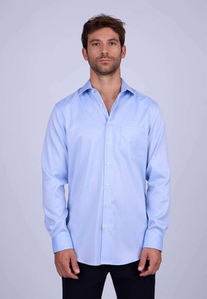 Chemise bleu clair à manches longues avec un col pointu, une poche avant et une fermeture à boutons. Texture de tissu lisse, coupe ajustée.