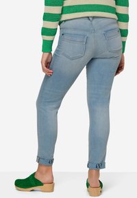 Jeans de color azul claro con un corte ajustado, que presentan dos bolsillos traseros, puños enrollados y un acabado sutilmente texturizado. Combinados con zuecos verdes.