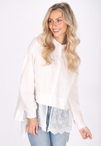 Witte button-up blouse met lange mouwen, voorzien van een kanten zoomontwerp. Zachte stof; verkorte pasvorm met ingewikkelde kanten details aan de onderkant.