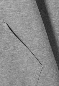 Gros plan d'une poche en tissu gris avec coutures visibles et texture douce, probablement partie d'un vêtement.