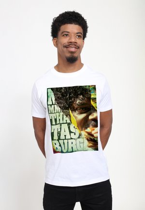 Hvid bomulds-T-shirt med et farverigt grafisk print af en person, der spiser, med fed grøn tekst, der står "Mmm, det smager godt."