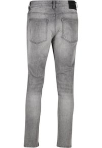 Vue de dos d'un jean gris slim avec deux poches arrière, passants de ceinture et patch de marque noir sur la taille.