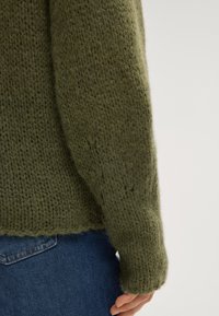 Pullover verde chunky lavorato a maglia con una finitura testurizzata, caratterizzato da una vestibilità rilassata e maniche a sbuffo, abbinato a jeans blu.